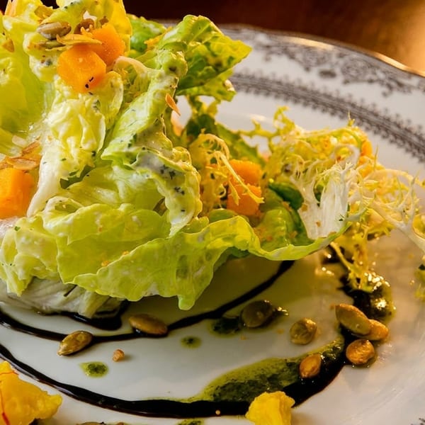Gourmet salad with fresh greens, butternut squash, pumpkin seeds, and balsamic glaze on a decorative plate.