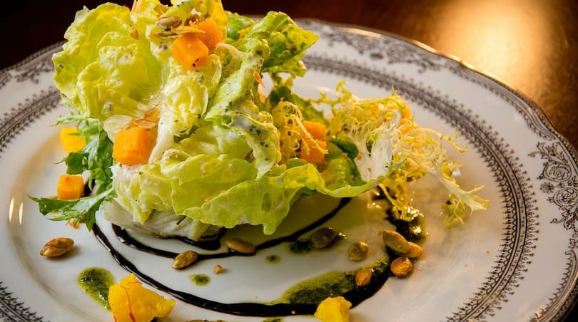 Gourmet salad with fresh greens, butternut squash, pumpkin seeds, and balsamic glaze on a decorative plate.